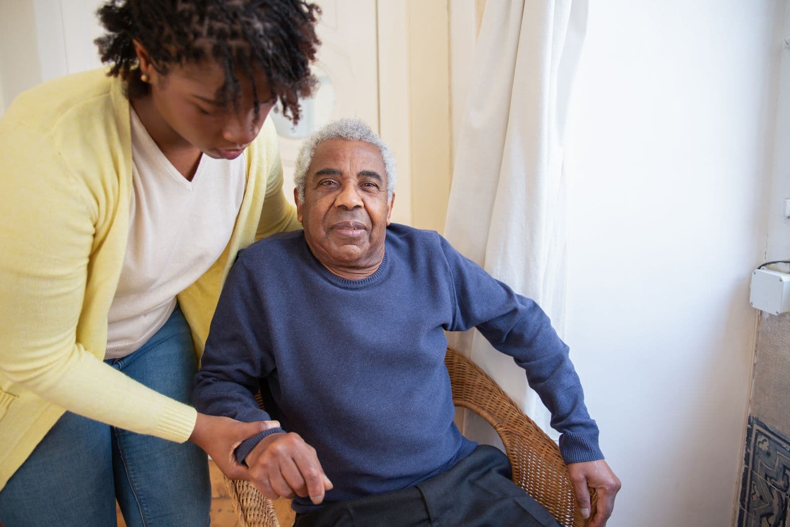 A support worker with her arm around an older man, both smiling at home