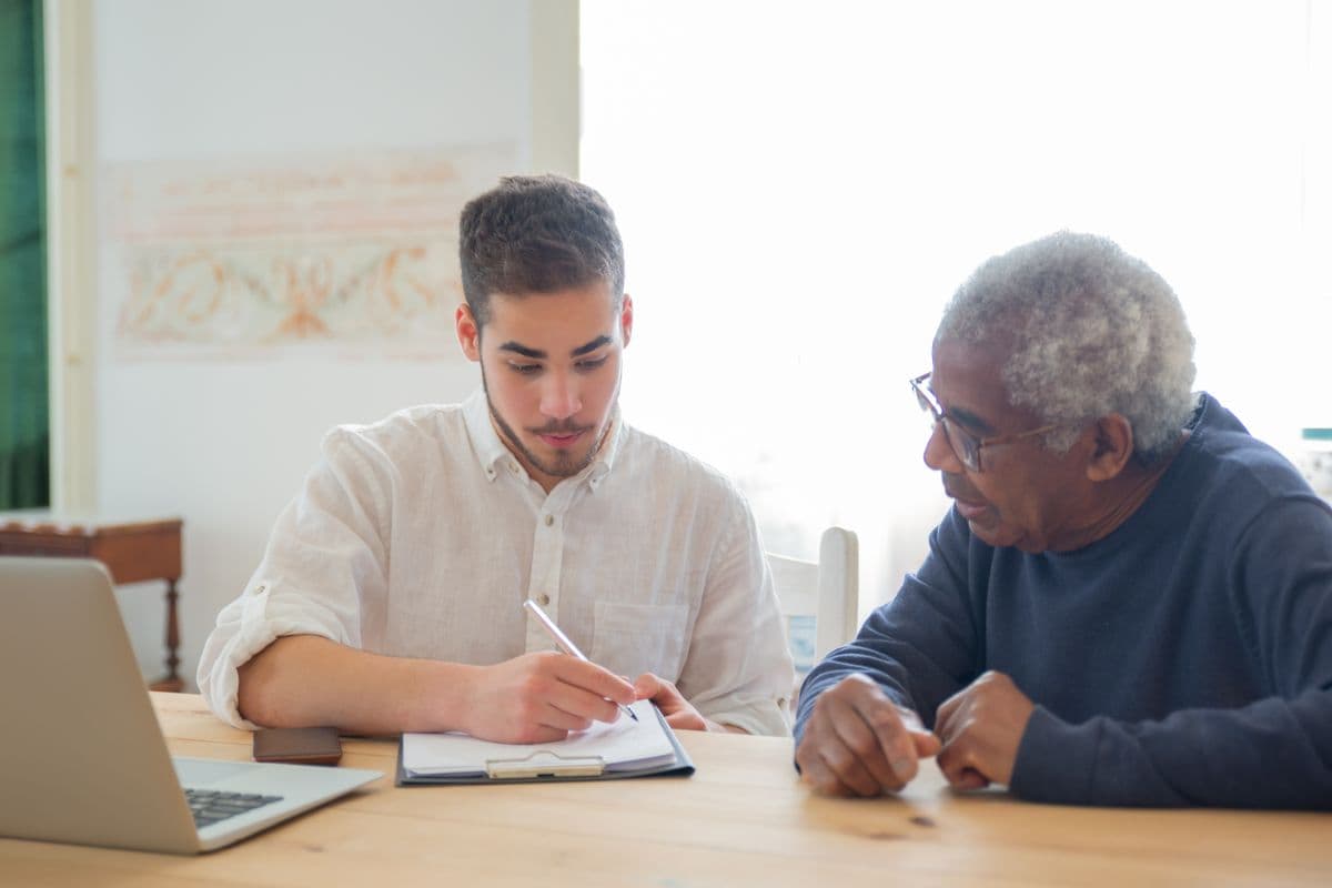 A support coordinator taking notes while talking through a plan with an older man